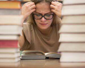 Mulher com expressão de cansaço e frustração tentando estudar idiomas com TDAH, entre pilhas de livros, simbolizando dificuldade de foco e concentração.
