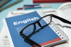 Livro de inglês com óculos sobre a mesa, representando por que o brasileiro tem tanta dificuldade em falar inglês